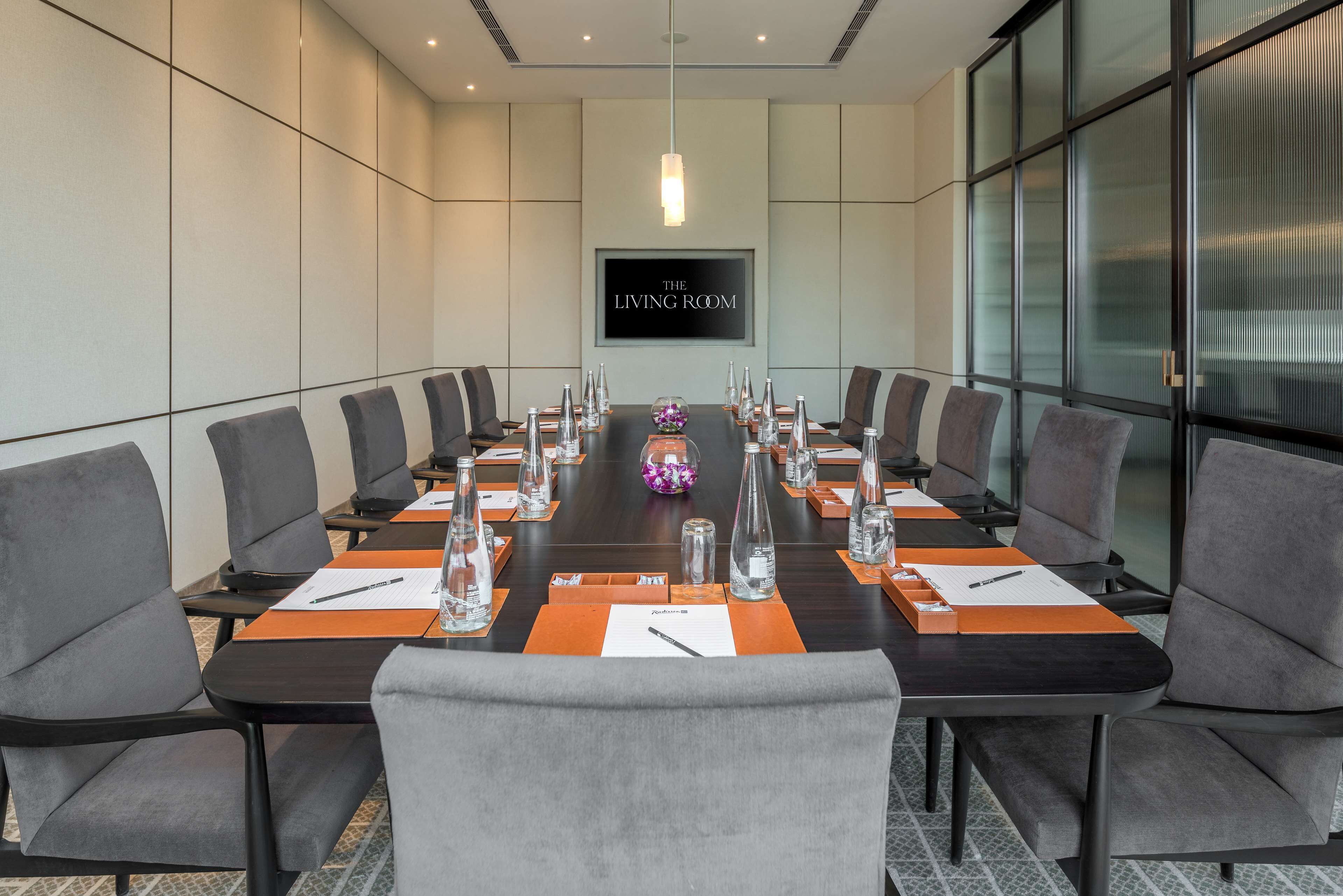 A conference room with a long table, chairs, water bottles, and a large screen displaying "THE LIVING ROOM".