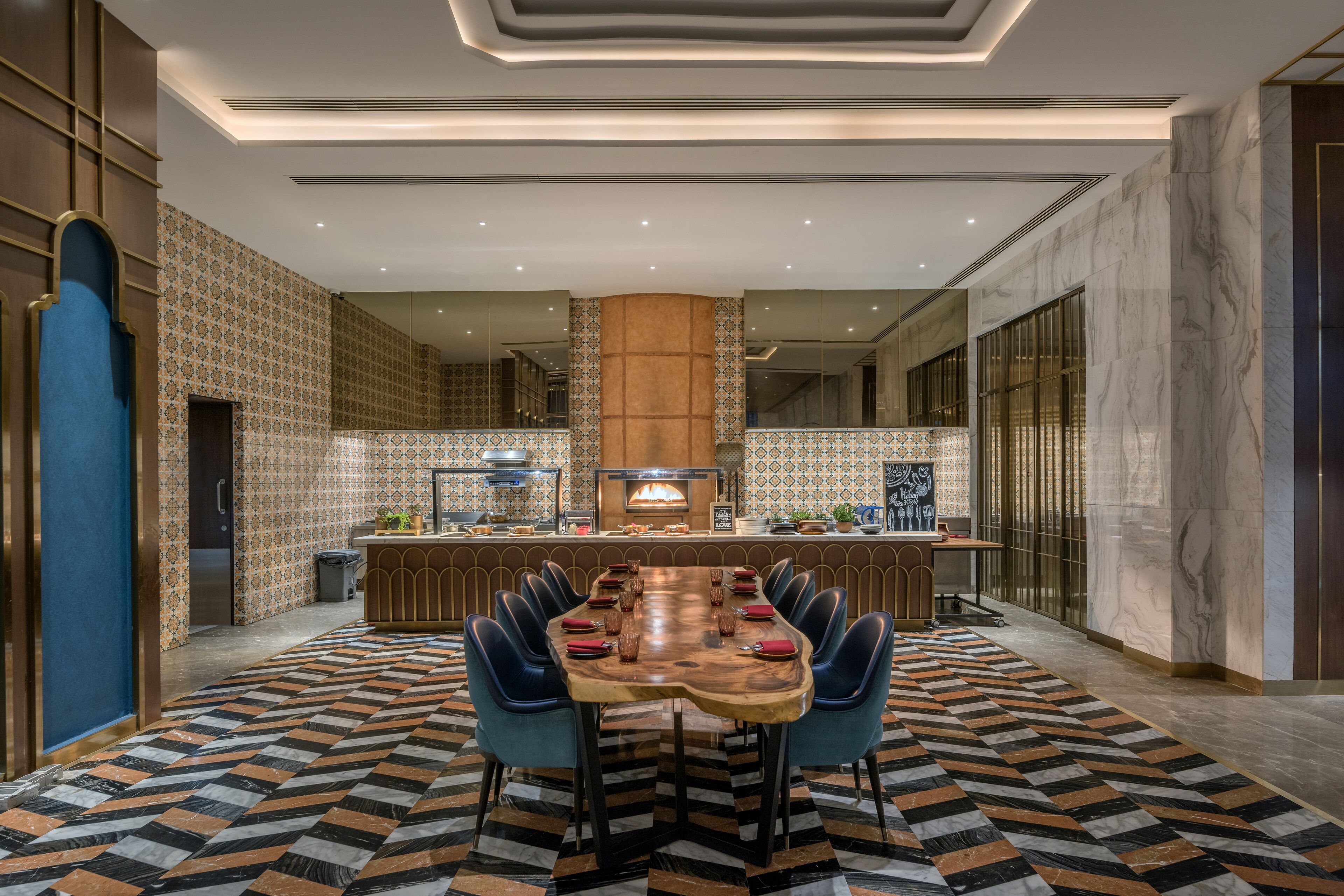 A modern dining area with a long wooden table, blue chairs, and a patterned floor.