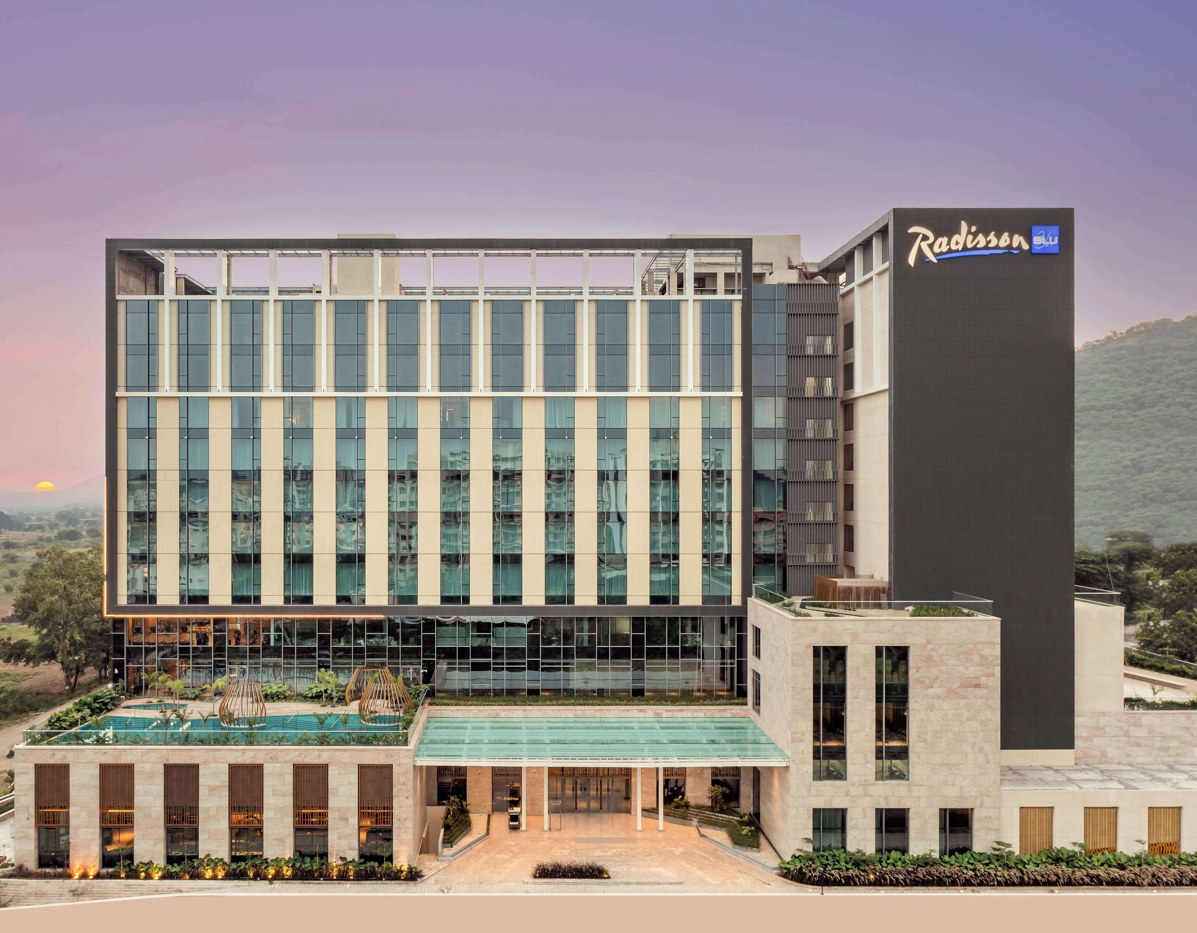 Un hotel Radisson moderno con una amplia fachada de vidrio, una piscina en la azotea y un área de entrada ajardinada.