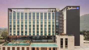 Un hotel Radisson moderno con una amplia fachada de vidrio, una piscina en la azotea y un área de entrada ajardinada.