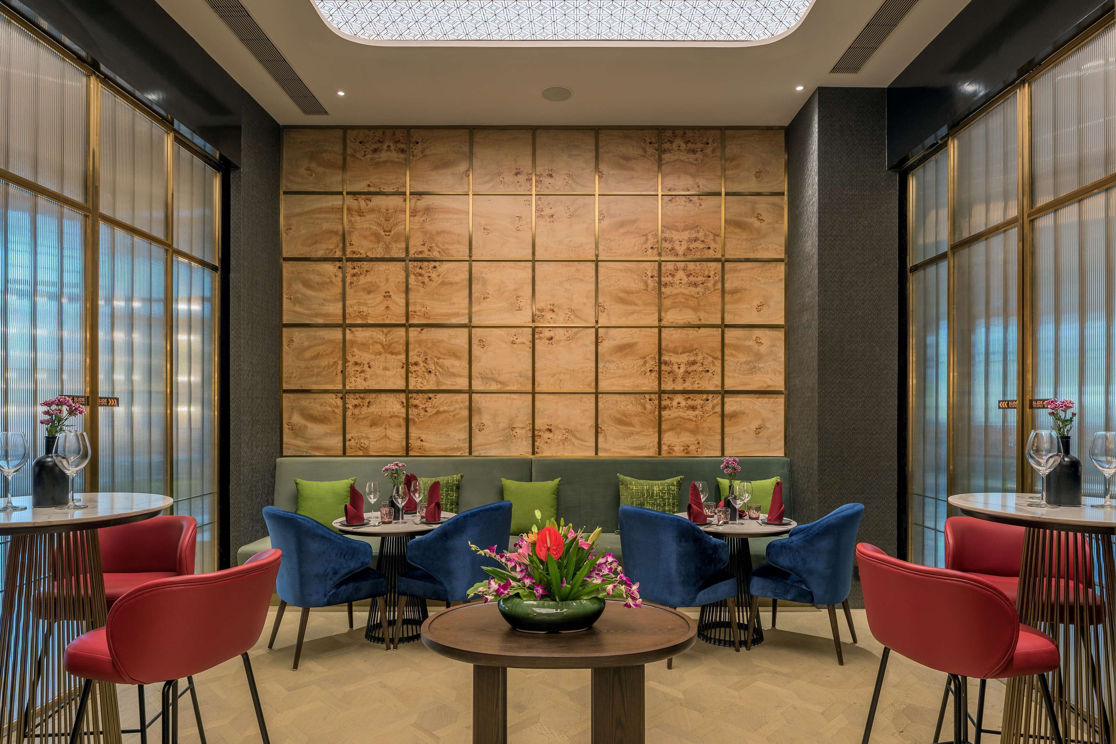 A modern dining area with round tables, red and blue chairs, and a central floral arrangement.