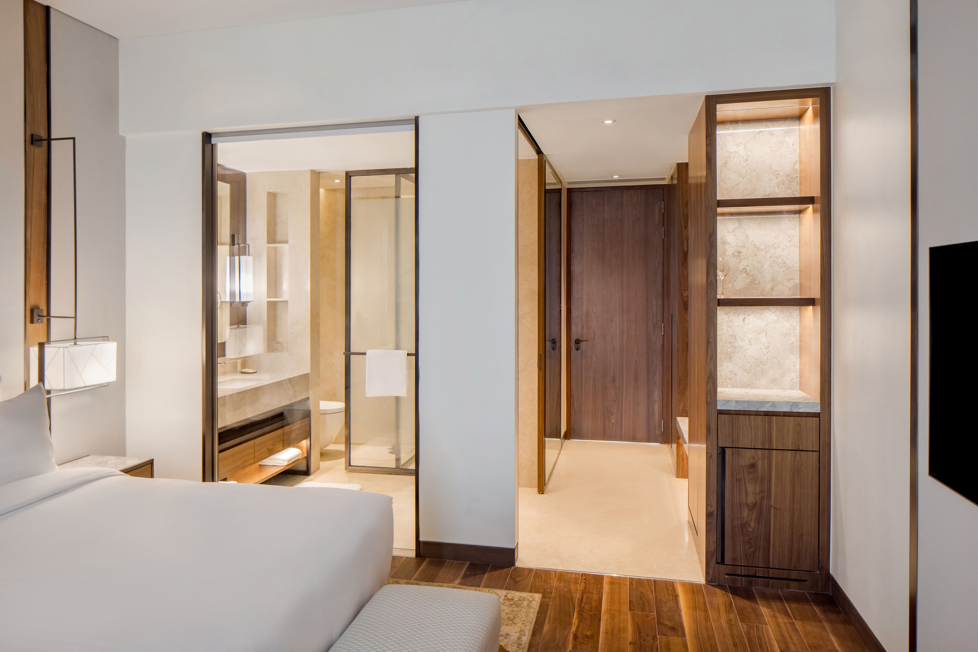 Una habitación de hotel moderna con una cama grande, un vestidor amplio y un baño con cabina de ducha de vidrio.