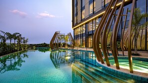 Et moderne hotel med swimmingpool, veloplyst facade og klar himmel.