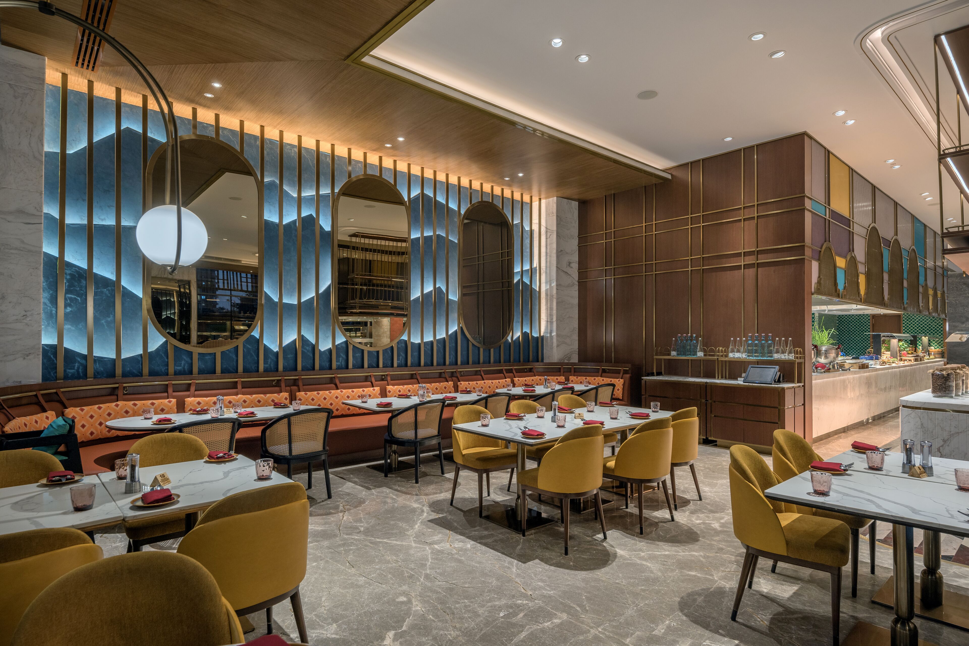 En modern restaurang med en lång bardisk, flera sittgrupper och en dekorativ vägg med speglar och vertikala ljuspaneler.