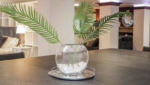 Un florero de vidrio transparente con guijarros blancos y dos hojas de helecho verde sobre un posavasos redondo.