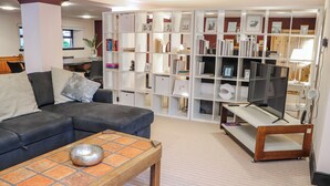 Una sala de estar con un sofá modular, una mesa de centro, un televisor sobre un mueble bajo y una estantería llena de libros y objetos decorativos.