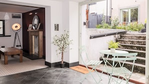 Un interior moderno con un escritorio de madera, una lámpara de pie, una planta en maceta y vistas al balcón exterior.