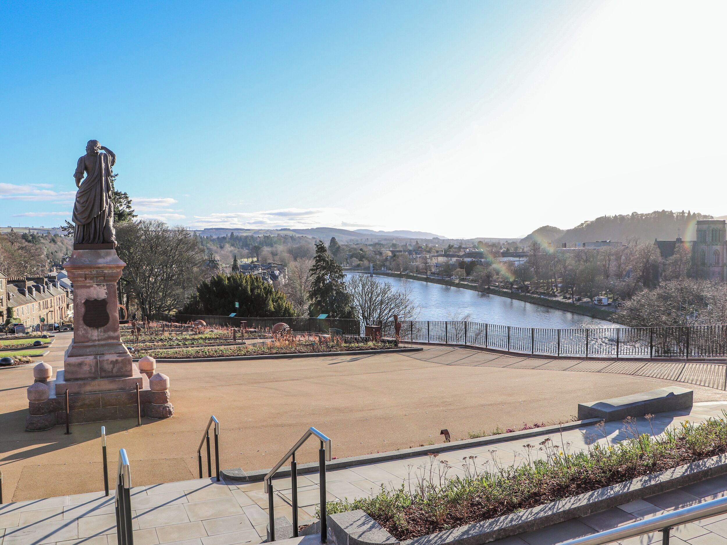 A statue in a park with a river and buildings in the background.
