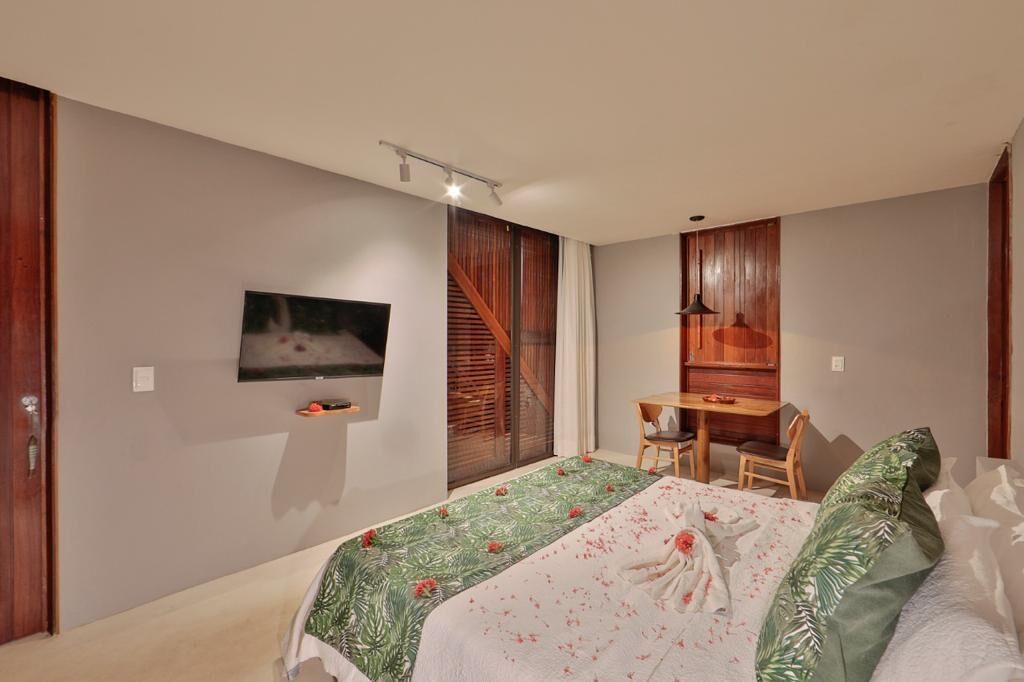 Un dormitorio moderno con cama, televisor montado en la pared, escritorio con silla y ventana con persianas de madera.