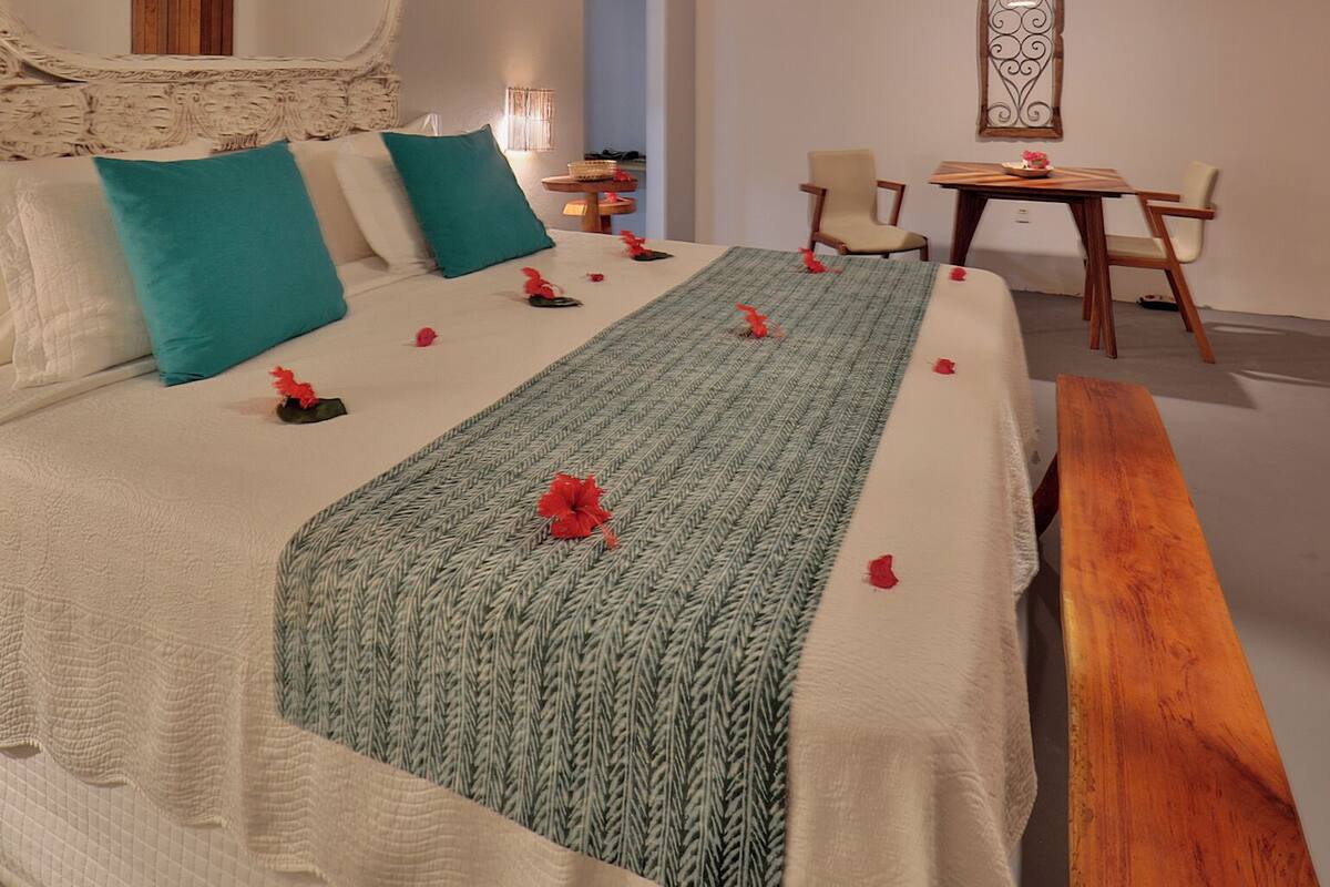 A neatly arranged bedroom with a large bed, a bedside table, a chair, and a hanging light fixture.