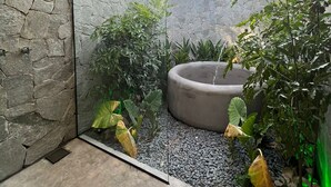 A modern outdoor space with a stone wall, a circular water feature, and tropical plants. - Villas Taturé (São Miguel dos Milagres)