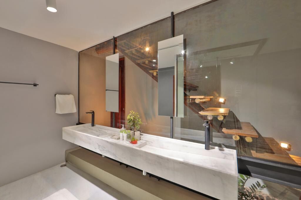 Un baño moderno con tocador de mármol, un espejo grande y cerramiento de vidrio para una escalera de madera.
