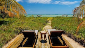 A wooden deck leading to a beach with two sun loungers and a small table. - Villas Taturé (São Miguel dos Milagres)