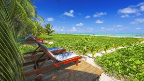 A wooden deck with two lounge chairs overlooking a beach with lush greenery and a clear blue sky. - Villas Taturé (São Miguel dos Milagres)