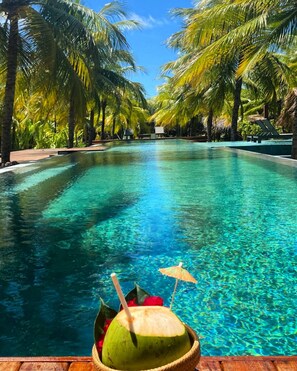 Una piscina cristalina rodeada de palmeras, con una bebida de coco en el borde.