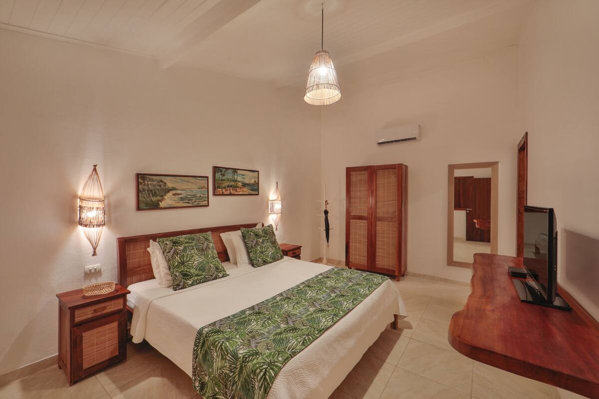 A bedroom with a bed, bedside lamps, a wooden wardrobe, a television, and artwork on the wall.