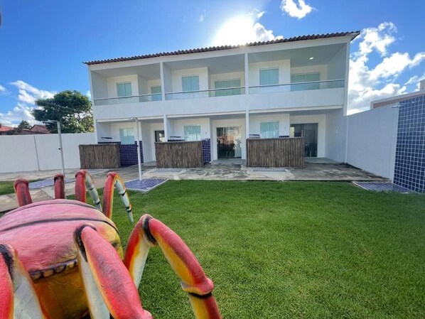 Two-story building with a flat roof and balcony, surrounded by a well-maintained lawn and a fence.