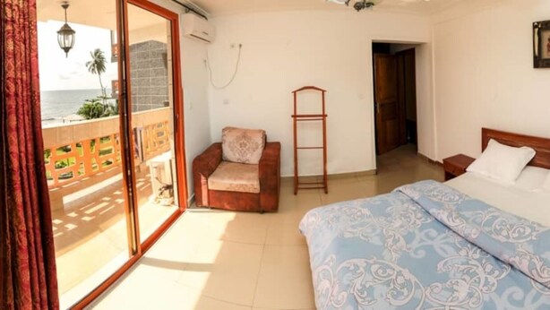 A bedroom with a bed, a chair, a ladder, and a view of the ocean through a sliding door.