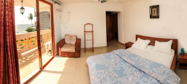 A bedroom with a bed, a chair, a ladder, and a view of the ocean through a sliding door.