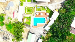 An aerial view of a property with a swimming pool, a patio area, and surrounding greenery.