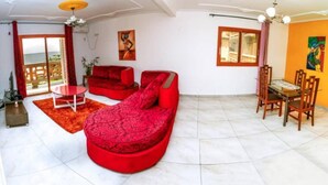 A spacious living area with a red sofa, a small table, and a dining set.