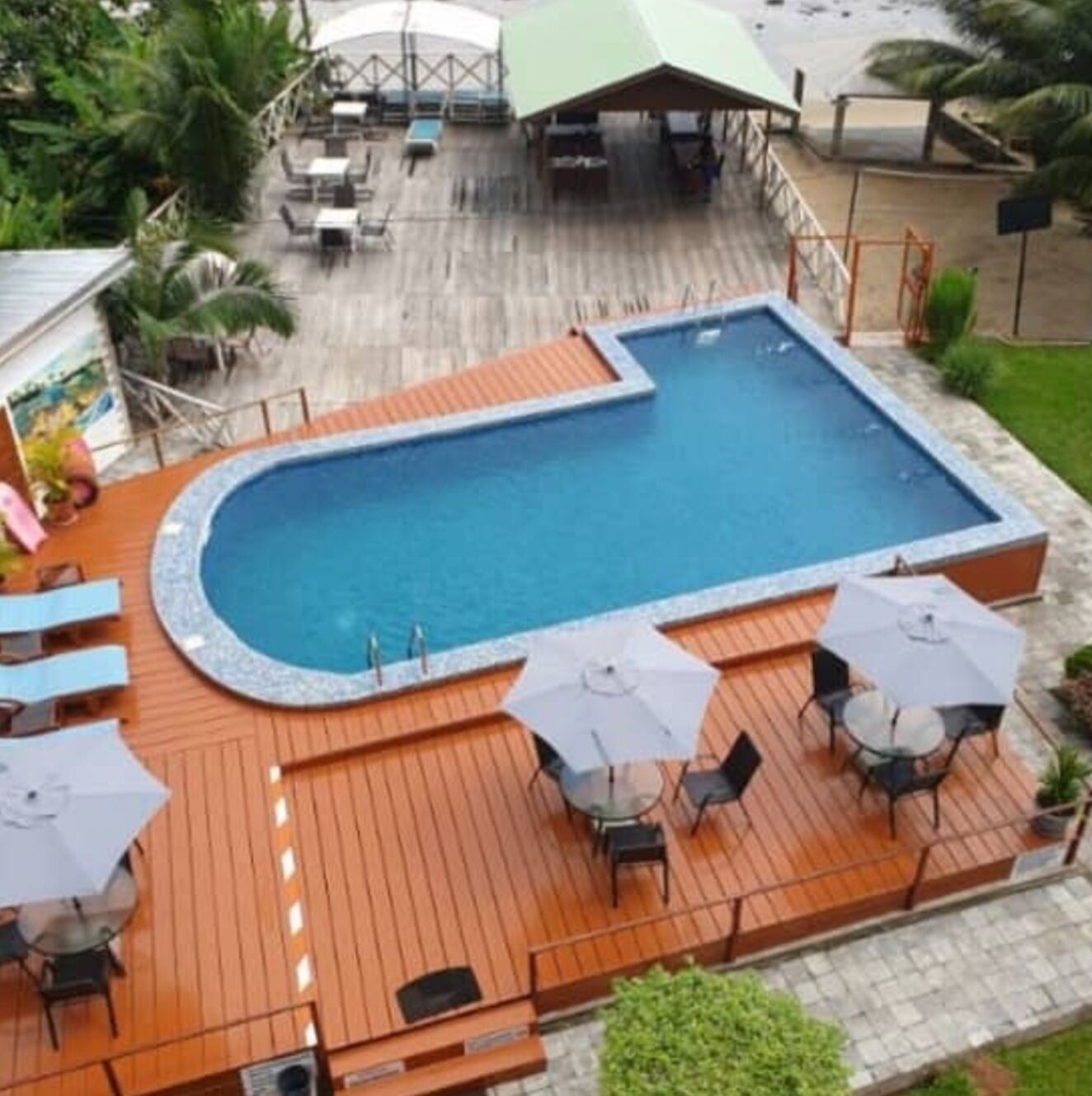 A pool area with a wooden deck, lounge chairs, and umbrellas.