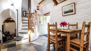 A rustic dining area with a wooden table and chairs, a staircase with a wooden railing, and a white wall with a framed picture. - Y Felin at Coed Cadw (Crymych)