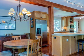 A modern kitchen with wooden cabinets, a stainless steel refrigerator, a dining table with chairs, and a chandelier. - Aspen Home - Pet Friendly, Private Hot Tub & Close to Bald Mountain Ski Lodge (Ketchum)