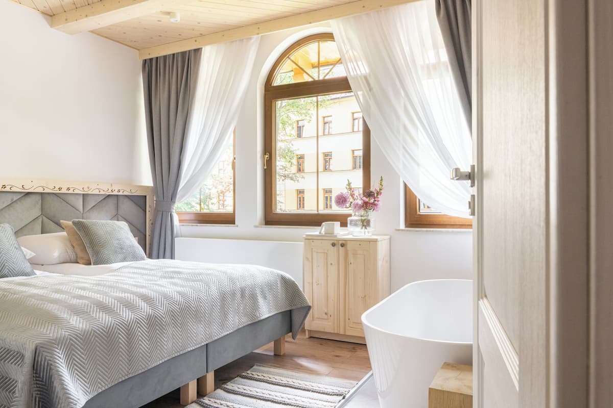Een slaapkamer met een bed, een houten kast, een raam met gordijnen en een bad.
