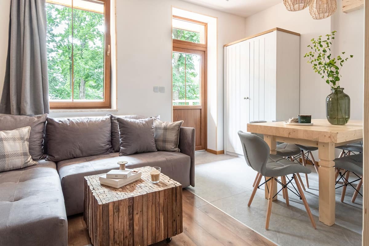 Een moderne woonkamer met een grijze bank, een houten salontafel, en een eethoek met een houten tafel en stoelen.