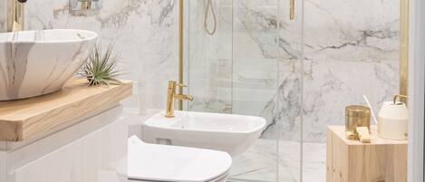 A modern bathroom with a white marble sink, a bidet, and a glass-enclosed shower area.