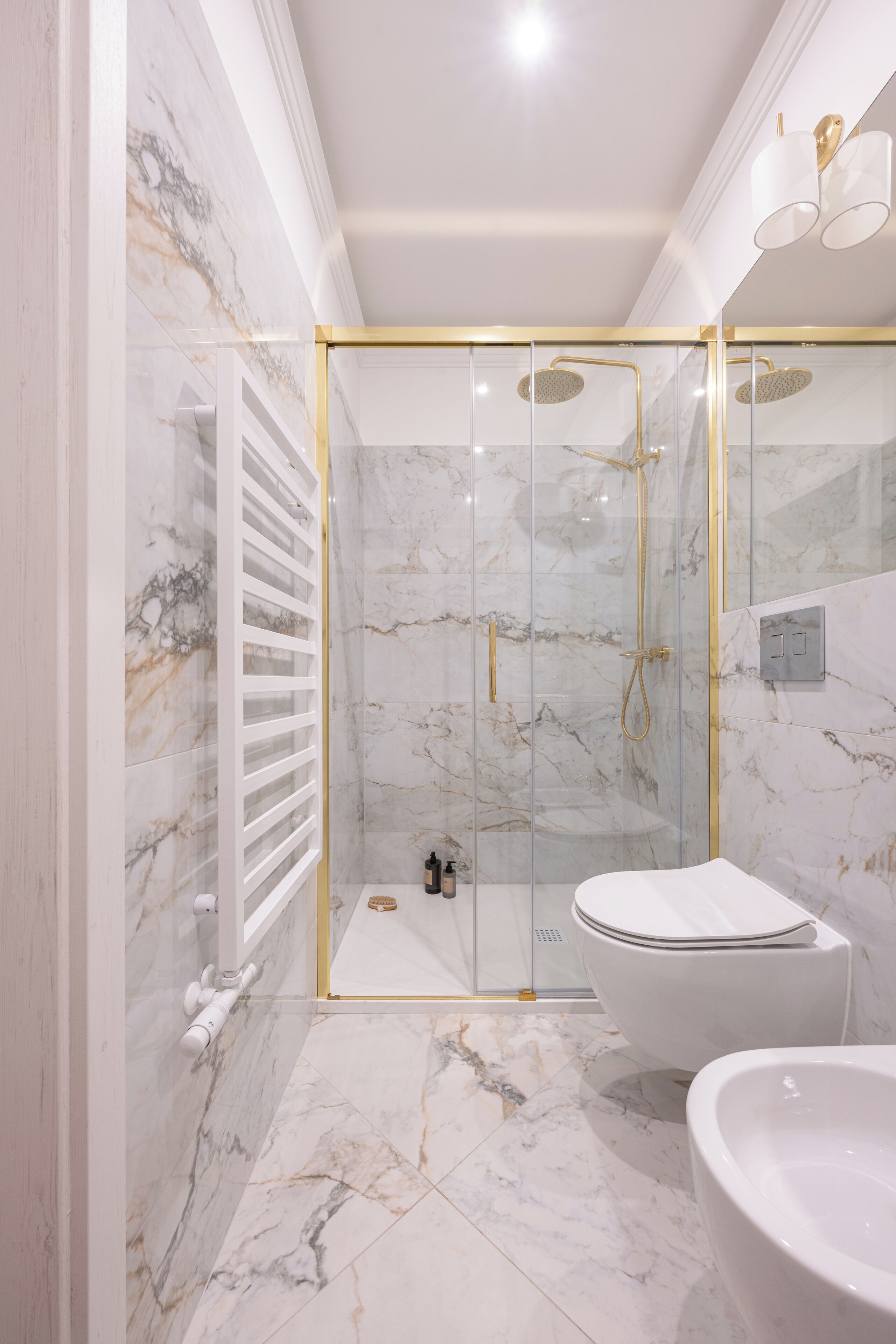 A modern bathroom with a glass-enclosed shower, a white bathtub, and marble walls.