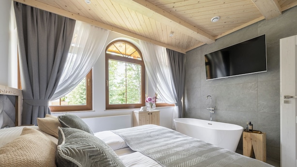 A modern bedroom with a large bed, a bathtub, and a TV mounted on the wall. - Apartamenty Villowe - Zakopane Centrum (Zakopane)
