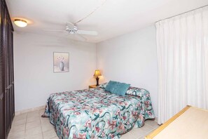 Ein Schlafzimmer mit einem Bett, einem Deckenventilator, einem Nachttisch mit Lampe, einem Bild an der Wand und einem Fenster mit Vorhängen.