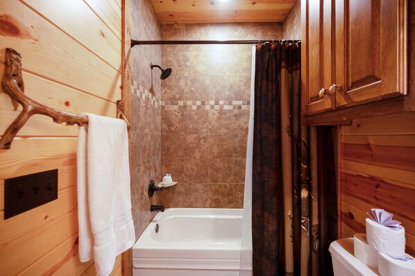 Une salle de bain rustique, avec des murs en bois, comprenant une baignoire, une douche et un porte-serviettes.