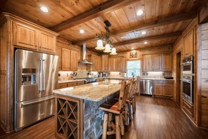 Une cuisine spacieuse avec des meubles en bois, un grand îlot central doté de tabourets, des appareils en acier inoxydable et un mur d’accent en pierre.