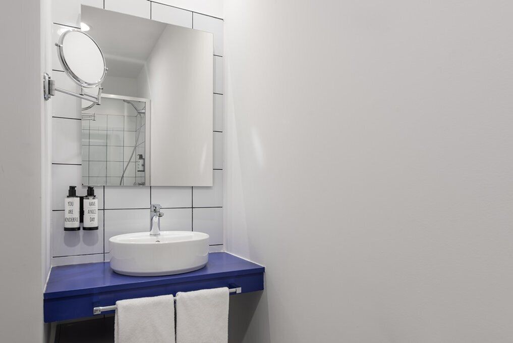Un baño con lavamanos blanco, encimera azul y espejo encima.