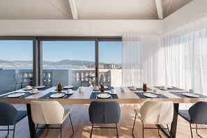 A dining area with a long table set for six, large windows offering a city view, and modern chairs. - Dorma Vigo (Vigo)
