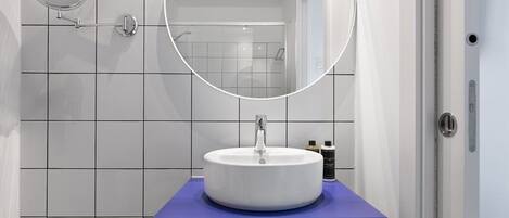 Un baño con lavamanos blanco, encimera azul y espejo redondo.