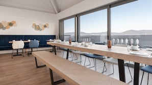 A modern dining area with a long table, benches, and chairs. There are decorative wall art pieces and a view of the sea through large windows. - Dorma Vigo (Vigo)