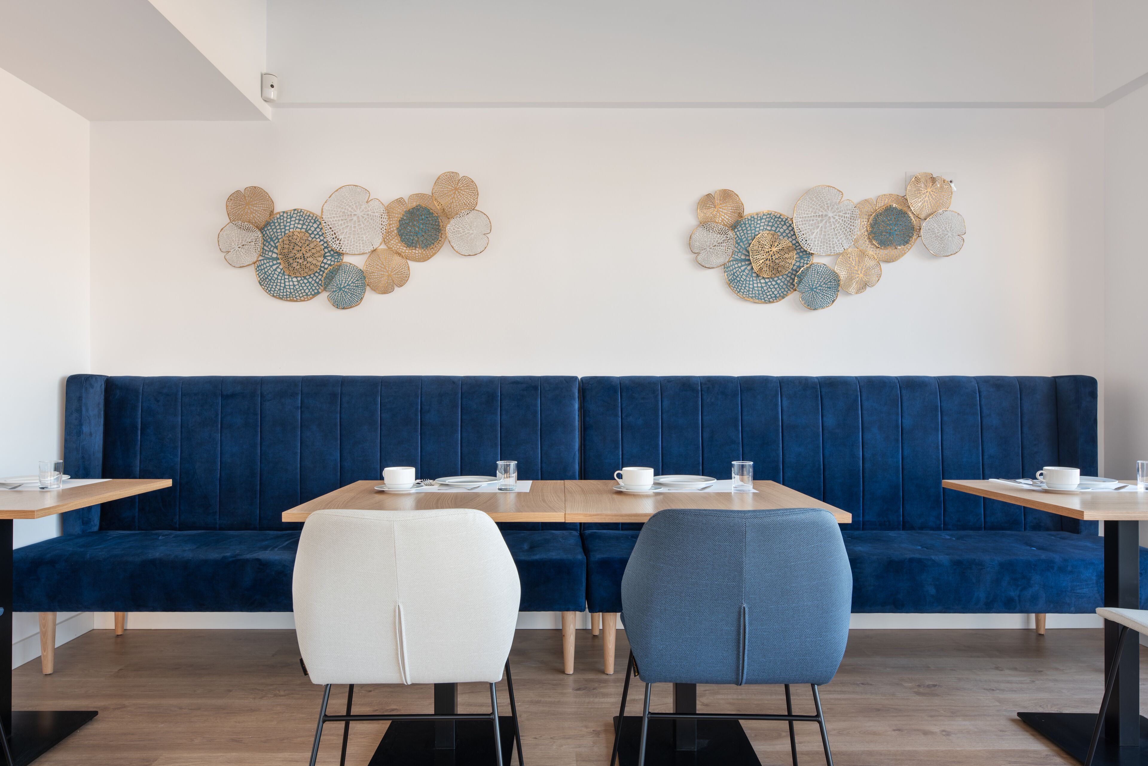 A modern dining area with a blue upholstered bench, two white chairs, and a wooden table set with white cups and glasses.