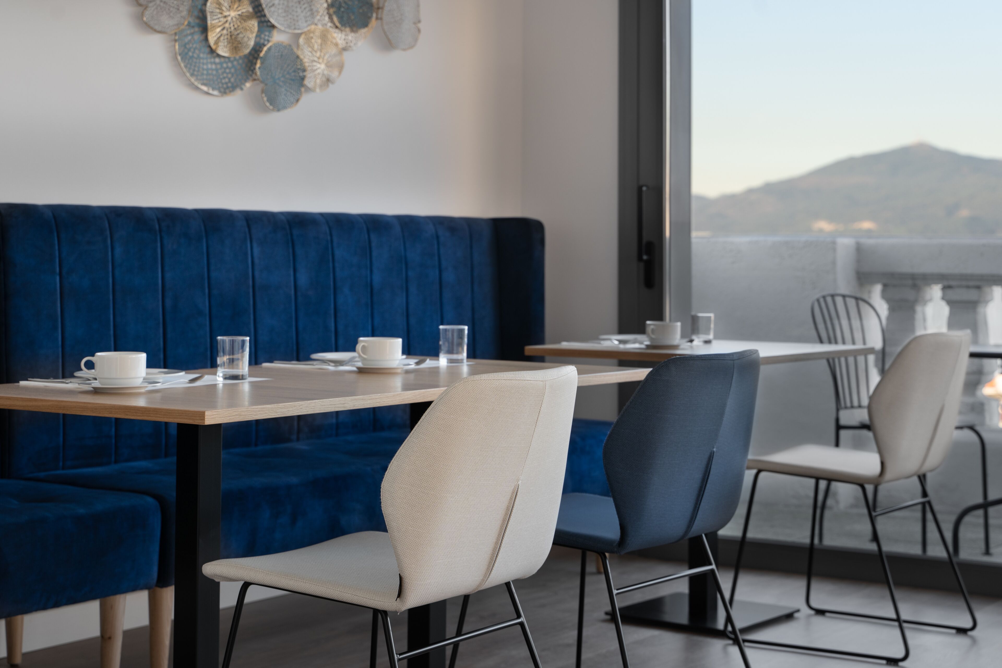 A modern dining area with a blue upholstered sofa, white chairs, and a table set with a cup and glass.