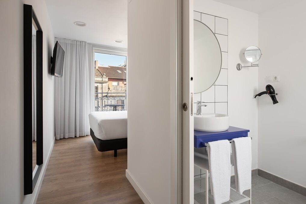 Habitación de hotel con cama, baño con lavamanos y espejo, y vistas al exterior.