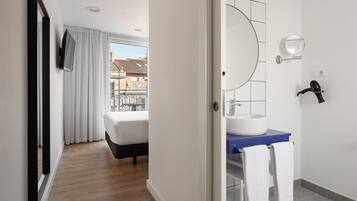 Habitación de hotel con cama, baño con lavamanos y espejo, y vistas al exterior.