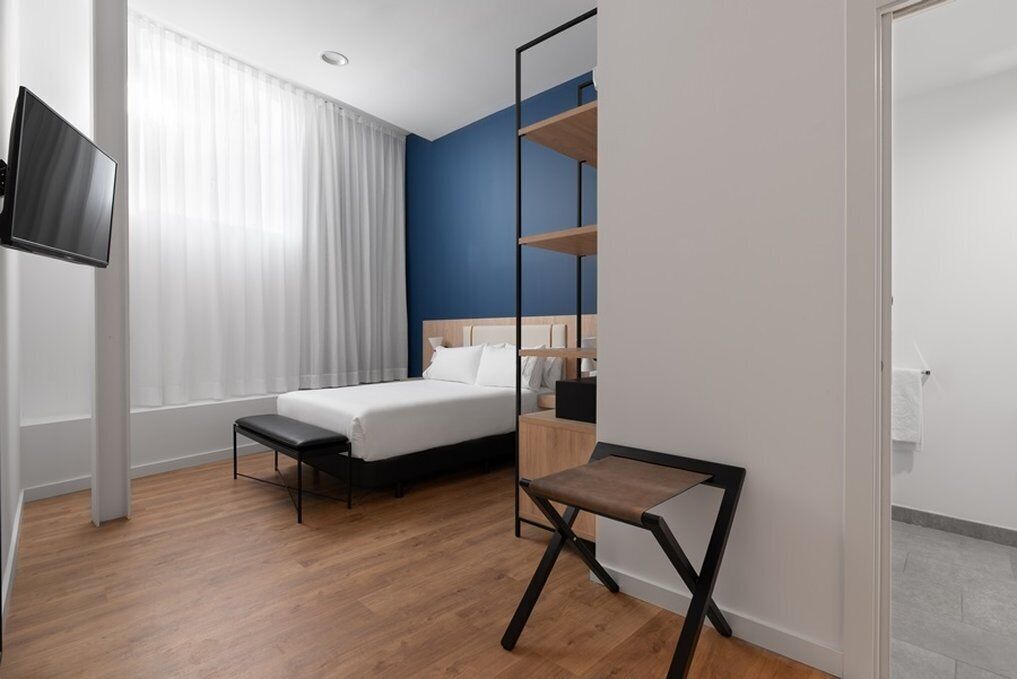 Una habitación de hotel con cama, televisión, escritorio y ventana con cortinas.