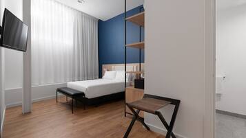 Una habitación de hotel con cama, televisión, escritorio y ventana con cortinas.