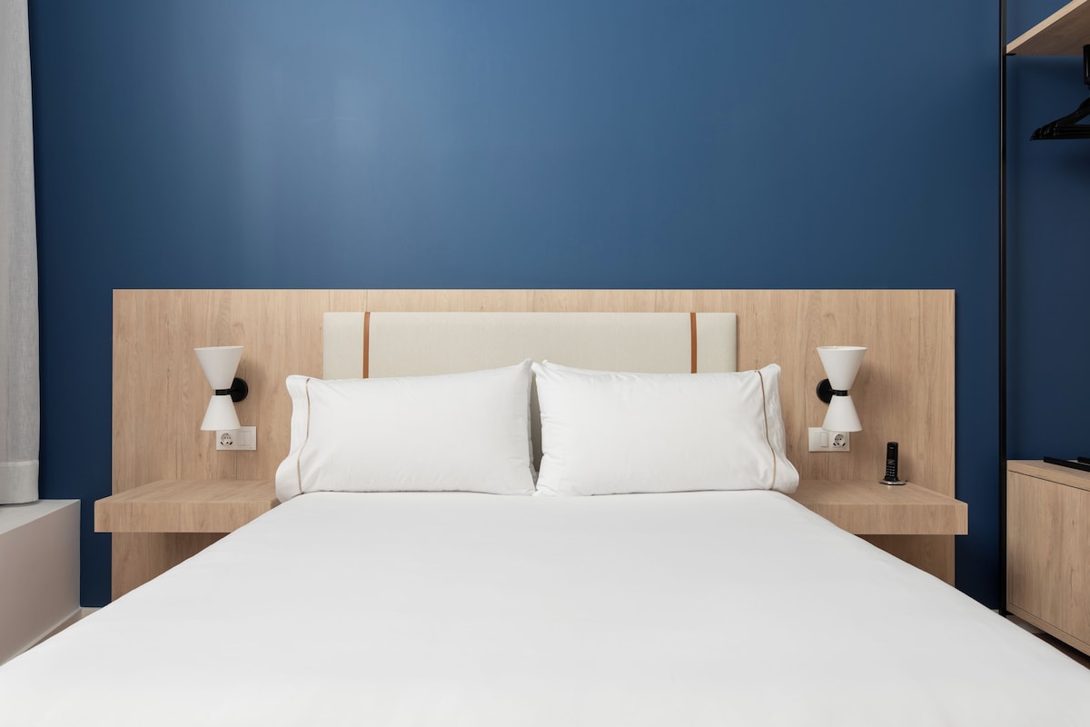 Habitación de hotel con cama, dos mesitas de noche y lámparas fijadas a la pared.