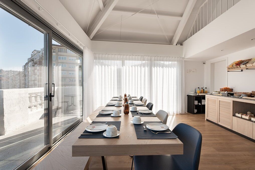 Un'elegante sala da pranzo con un lungo tavolo apparecchiato, ampie finestre e vista sulla città.