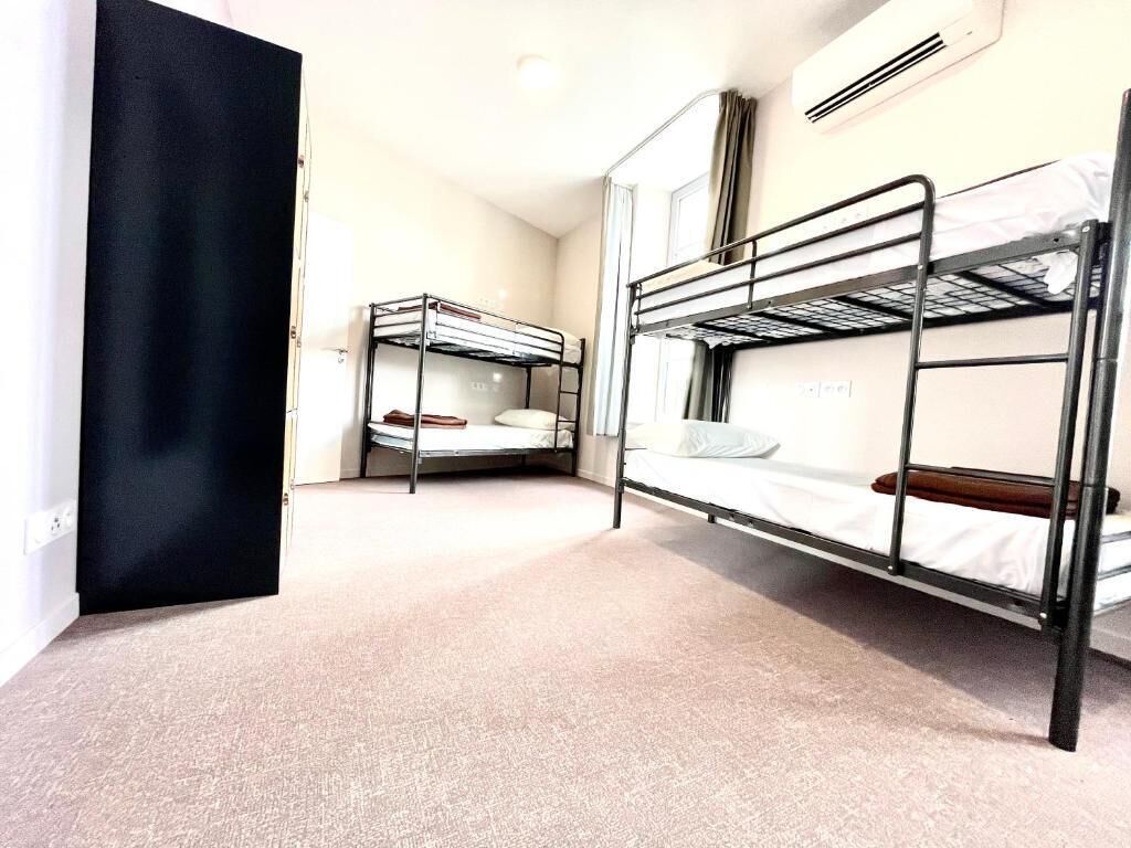 Una habitación con literas, una puerta negra y una ventana con cortinas.