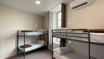 A room with two bunk beds, a window with curtains, an air conditioning unit, and a light switch on the wall.